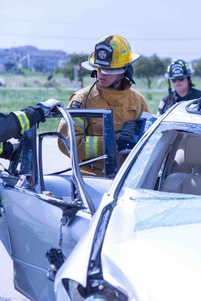 Firefighters using tools to rescue a person from a damaged vehicle at an accident scene.