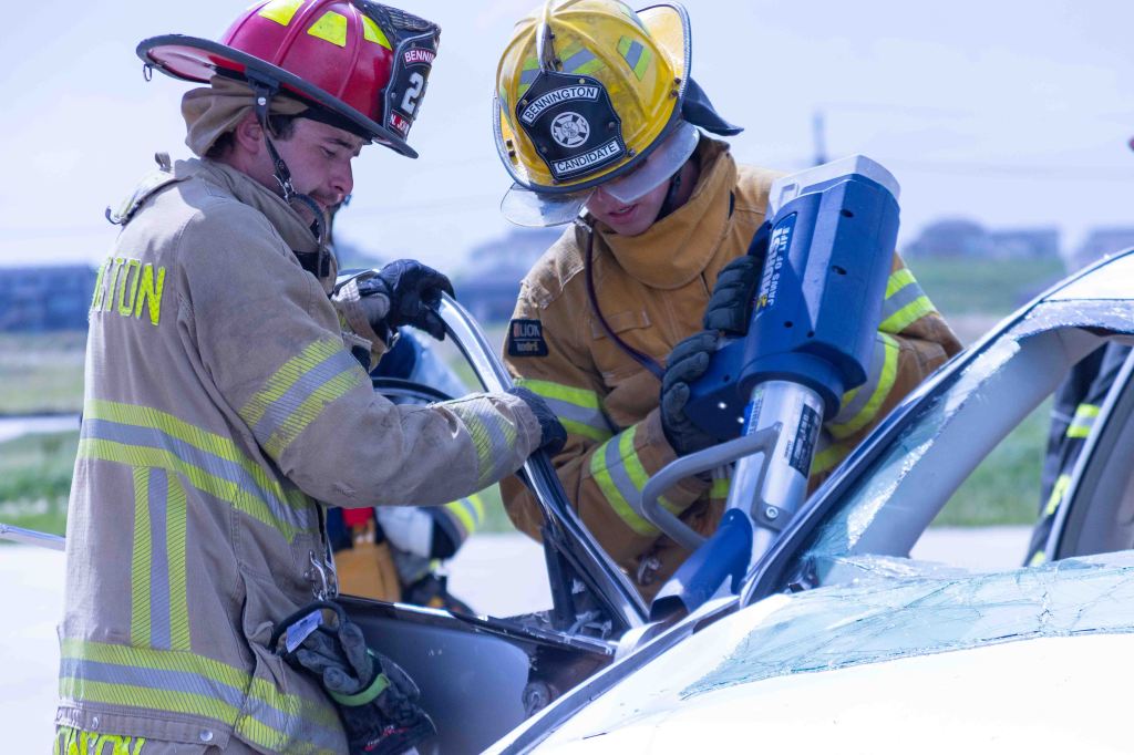 Two firefighters working together to extract a victim from a vehicle using specialized tools during a training exercise.