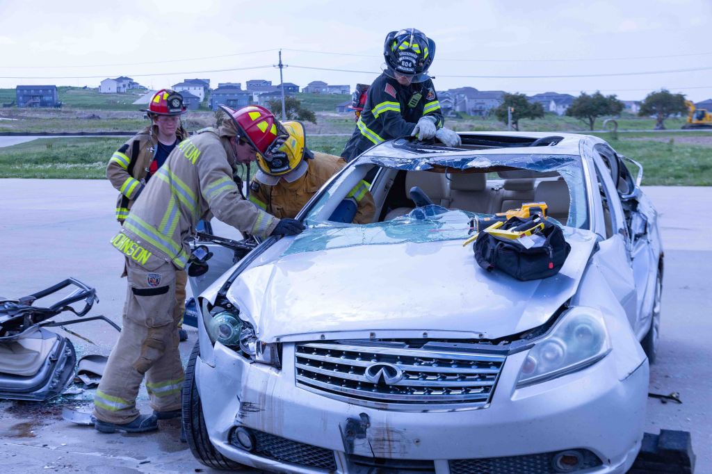 Firefighters working together to rescue a person from a damaged vehicle with a crushed roof.