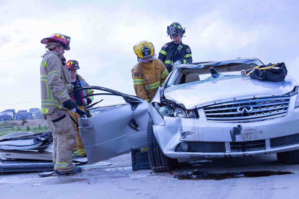 First responders working at the scene of a car accident, focusing on a damaged white vehicle.
