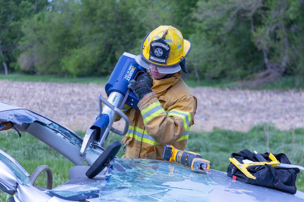 A firefighter in uniform using hydraulic rescue tools on a damaged car at an accident scene.