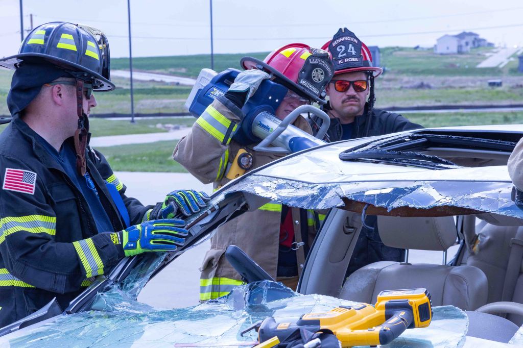 Firefighters using hydraulic tools to remove the roof of a damaged vehicle during a rescue operation.