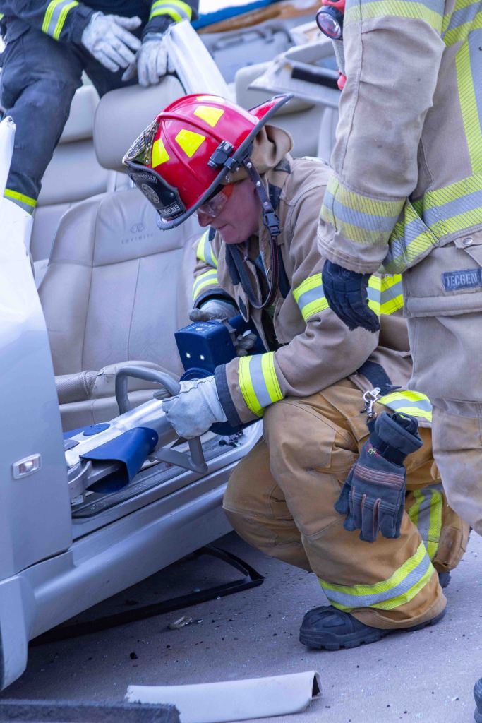 A firefighter using a hydraulic tool to rescue a person from a vehicle during an emergency response.