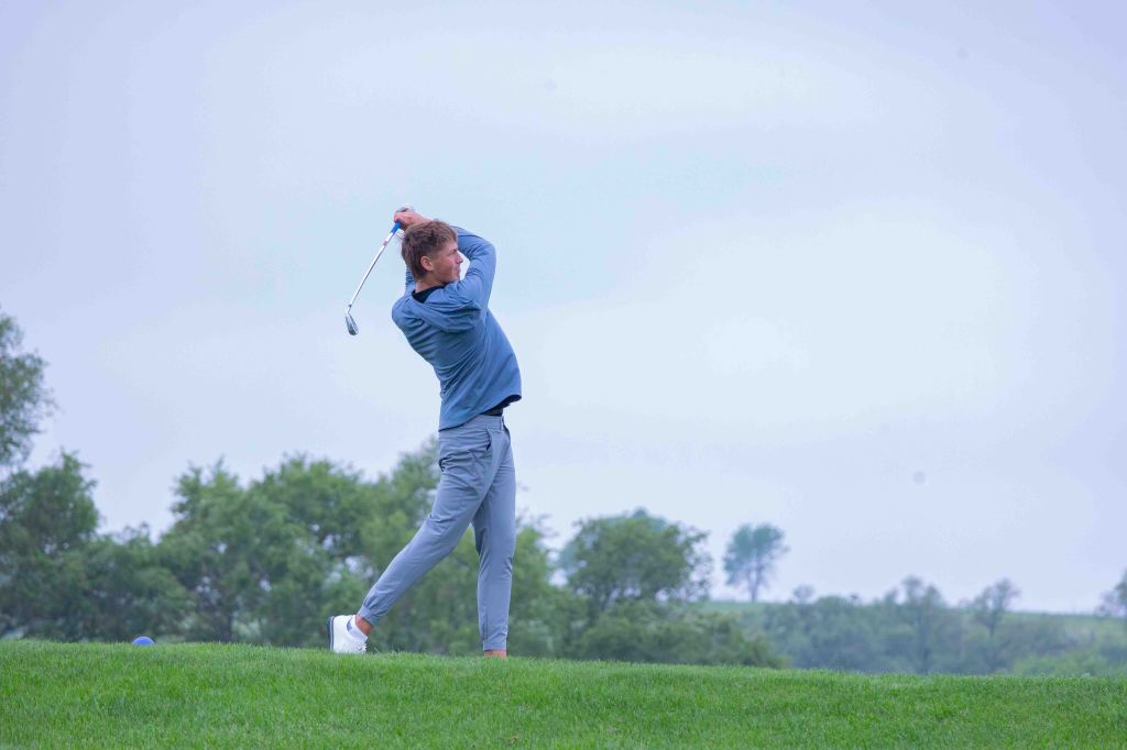 A golfer swinging a club on a grassy golf course under a cloudy sky.