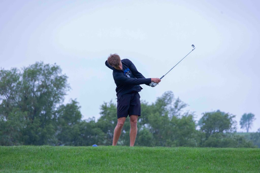 A young golfer executing a swing on a grassy course under a cloudy sky.