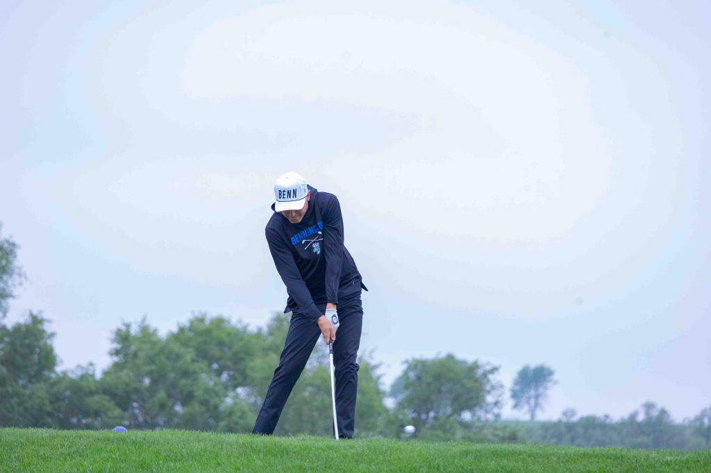 A golfer preparing to swing on a grassy course under a cloudy sky.