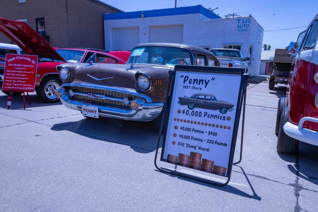 A vintage 1957 Chevy car named 'Penny' displayed at a car show, featuring a sign that lists the purchase price in pennies: 40,000 pennies for $400, weighing 220 pounds.