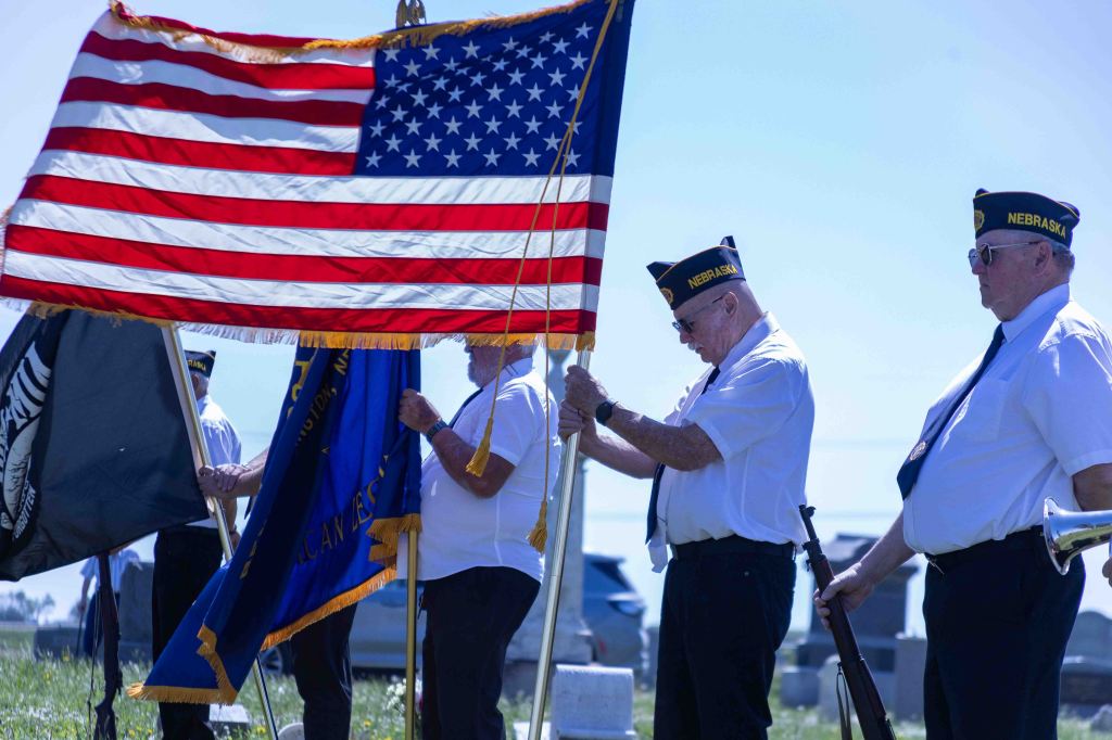 Veterans honor the American flag during a ceremony at a cemetery, with a focus on their uniforms and flags.