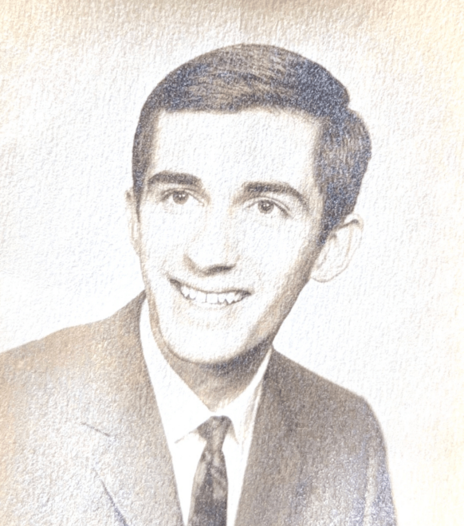 A vintage black and white portrait of a young man with a friendly smile, wearing a suit and tie.