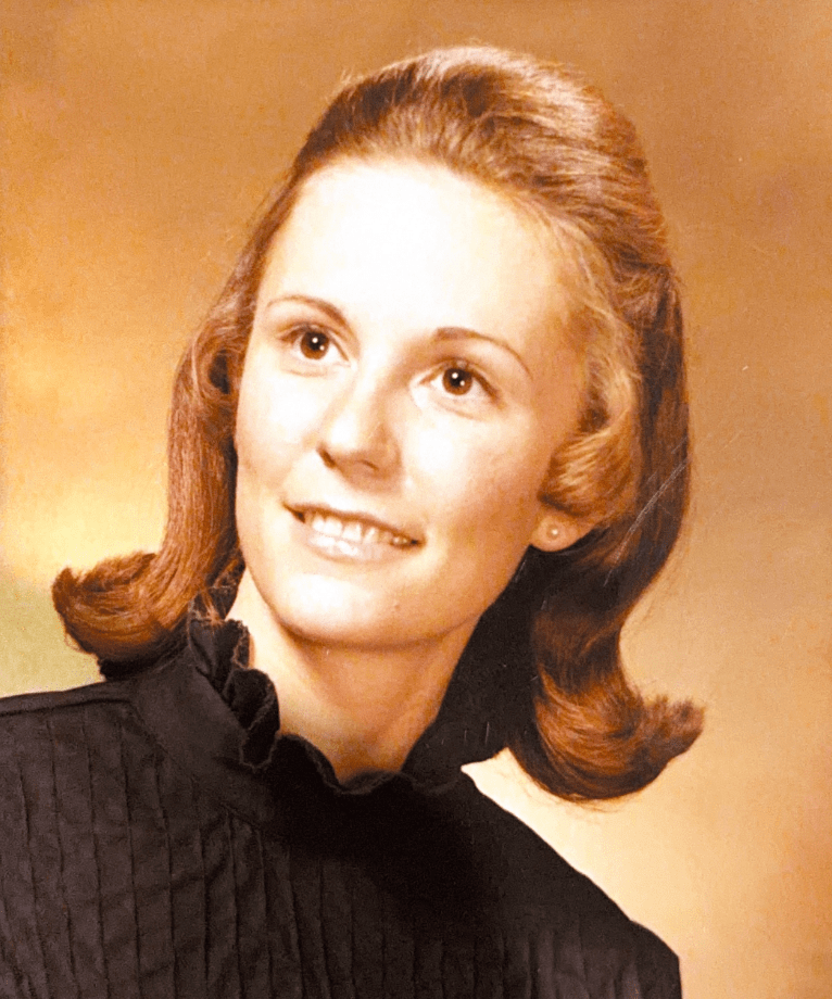 A portrait of a young woman with medium-length brown hair styled in soft waves, wearing a black textured blouse, smiling against a warm, gradient background.