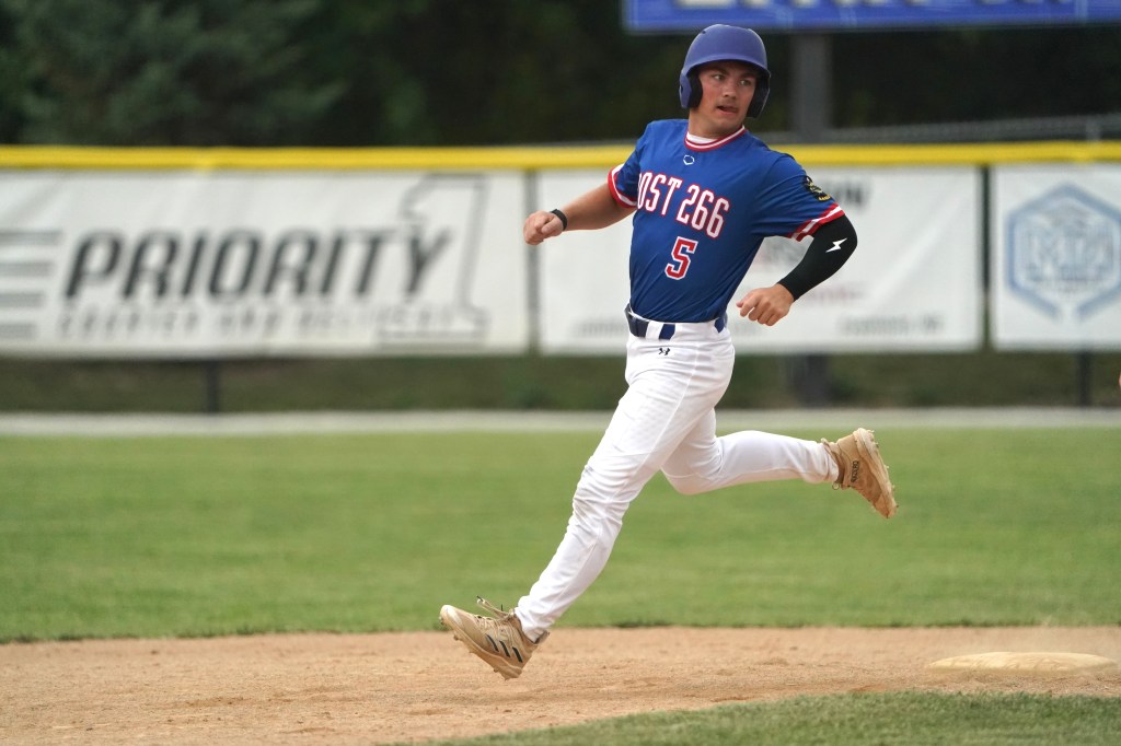 A young baseball player in a blue jersey with the number 5 running toward home plate on a baseball field.
