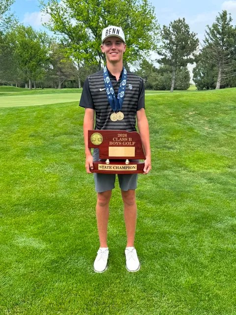 A young male golfer standing on a green lawn, holding a state champion plaque and wearing multiple gold medals.