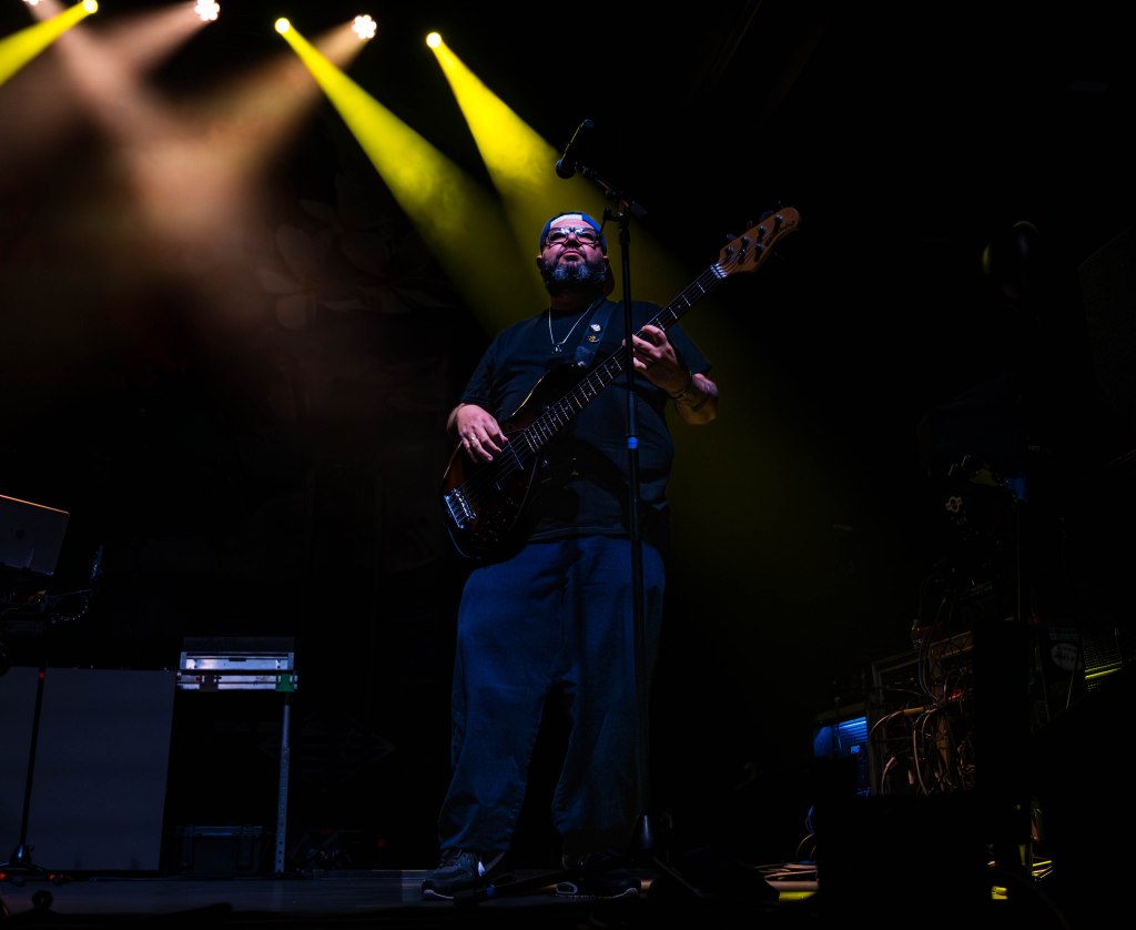A musician playing a bass guitar on stage under dramatic lighting.