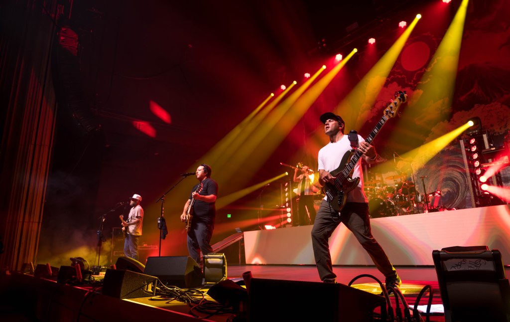 A live band performing on stage with vibrant lighting effects, featuring musicians playing guitar and bass, and an energetic atmosphere.
