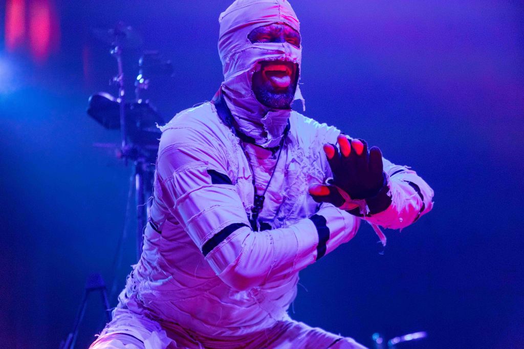 A performer dressed in a white, bandage-like costume, passionately expressing themselves on stage under dramatic lighting.