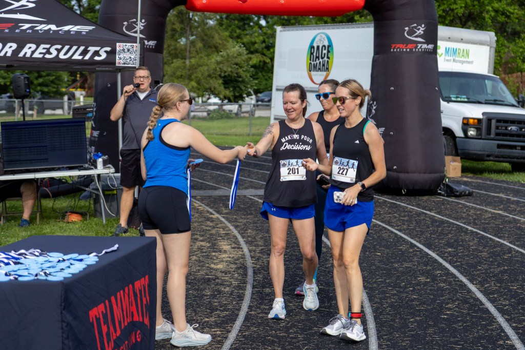 Participants receiving awards after a race at a finish line, with a digital display and event banner in the background.