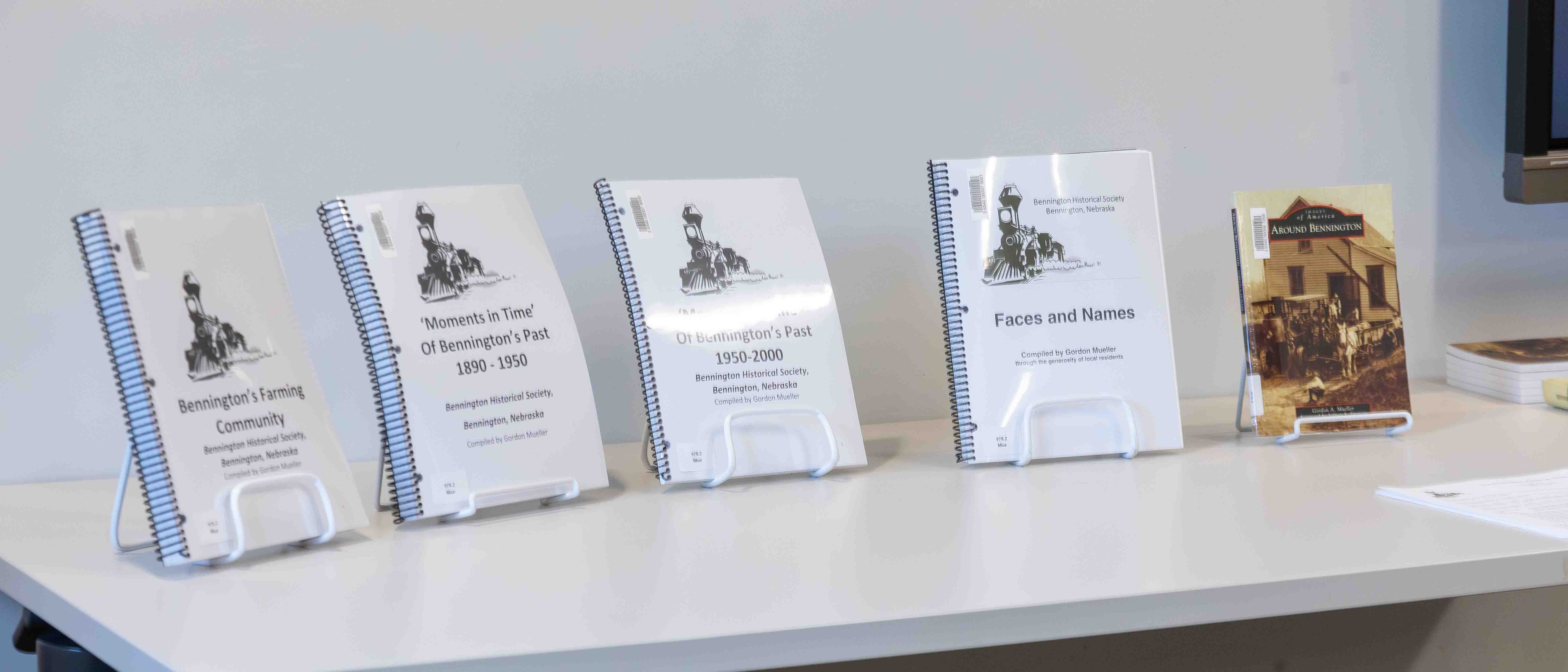 A collection of historical books displayed on a table, including titles such as 'Bennington's Farming Community', 'Moments in Time Of Bennington's Past 1890-1950', 'Moments in Time Of Bennington's Past 1950-2000', and 'Faces and Names', along with a book titled 'Around Bennington'.