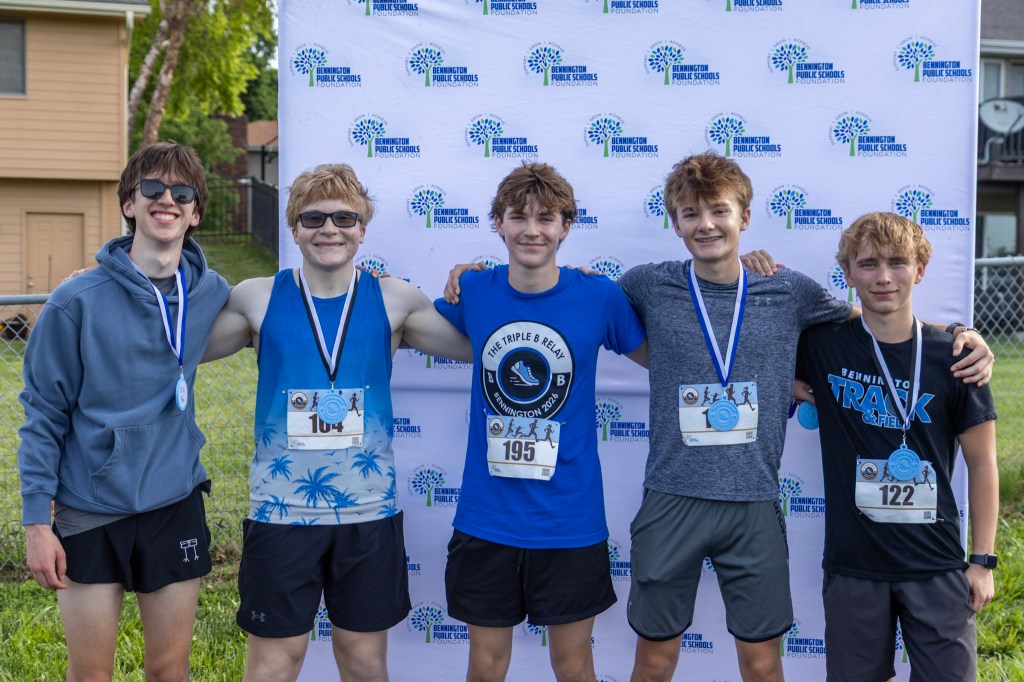 Five young athletes stand together, wearing medals and race bibs, in front of a branded backdrop from the Bennington Public Schools Foundation.