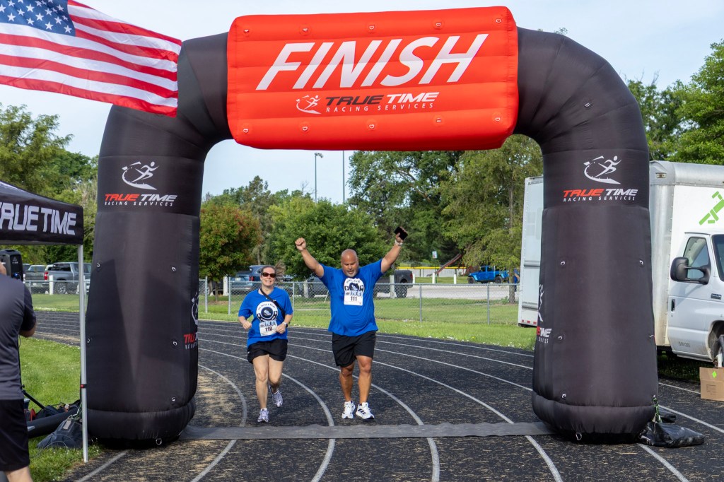 Runners crossing the finish line under a large inflatable finish arch during a race, with an American flag in the background.