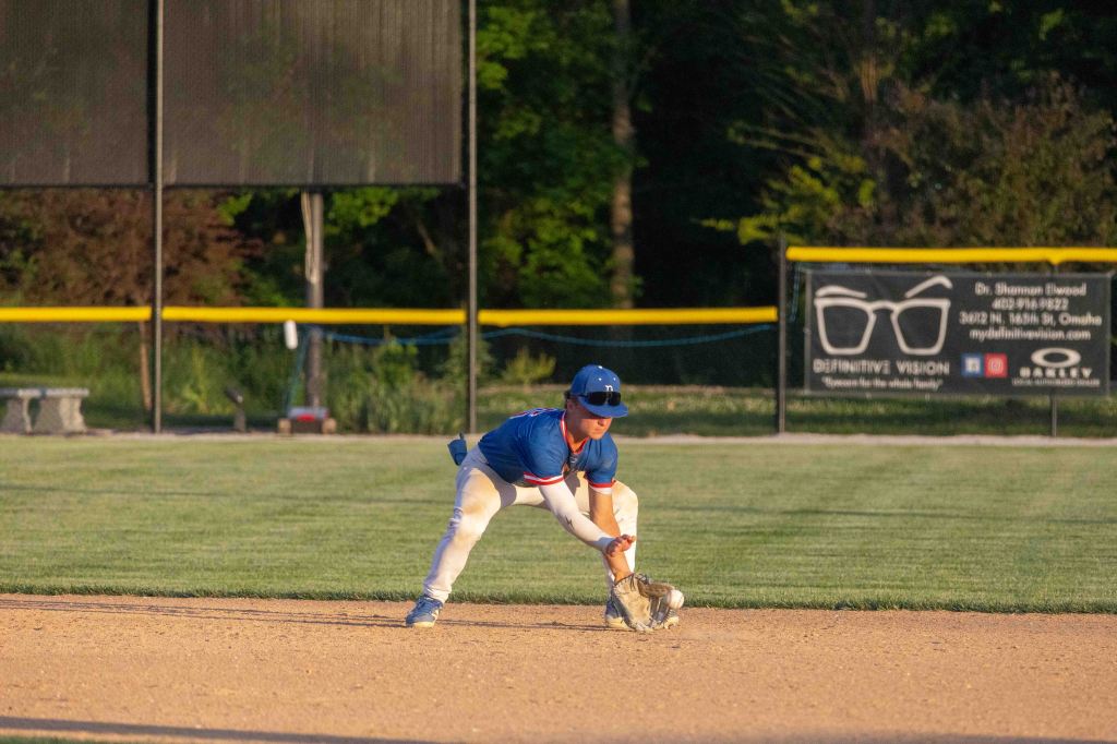 A young baseball player in a blue jersey fielding a ground ball during a game on a sunny day.