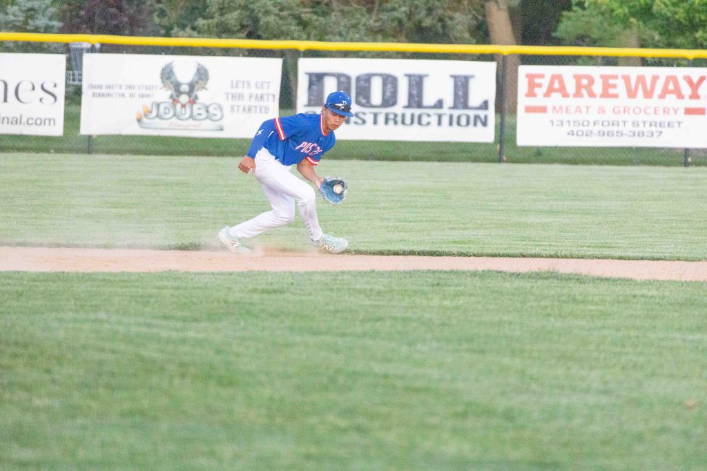 A baseball player in a blue uniform is fielding a ground ball on the infield grass during a game.
