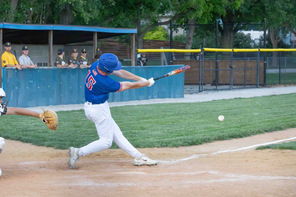 A baseball player in a blue jersey swings a bat at a ball on a baseball field, with spectators in the background.