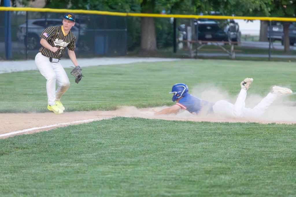 A baseball player in a blue uniform sliding into base, creating a cloud of dust, while another player in a striped shirt prepares to field the ball.