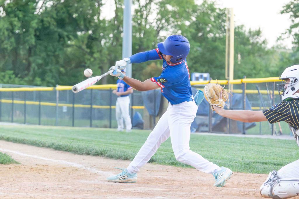 A young baseball player swings a bat at a baseball during a game, while a catcher prepares to receive the pitch.