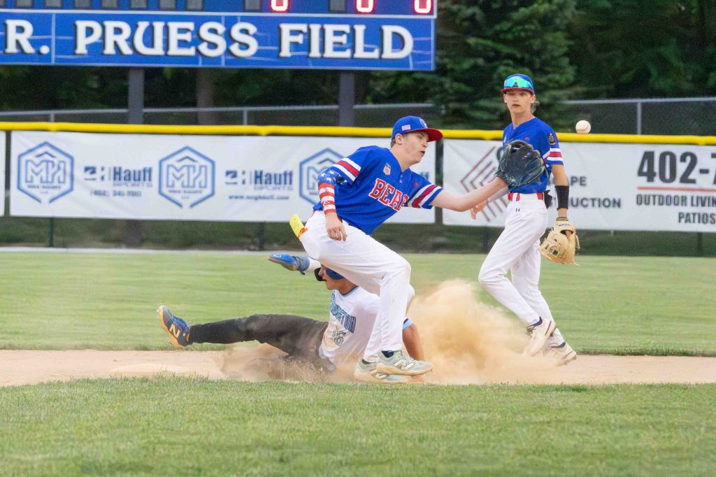 A baseball player attempting to field a ground ball while another player slides into the base, creating a cloud of dust.