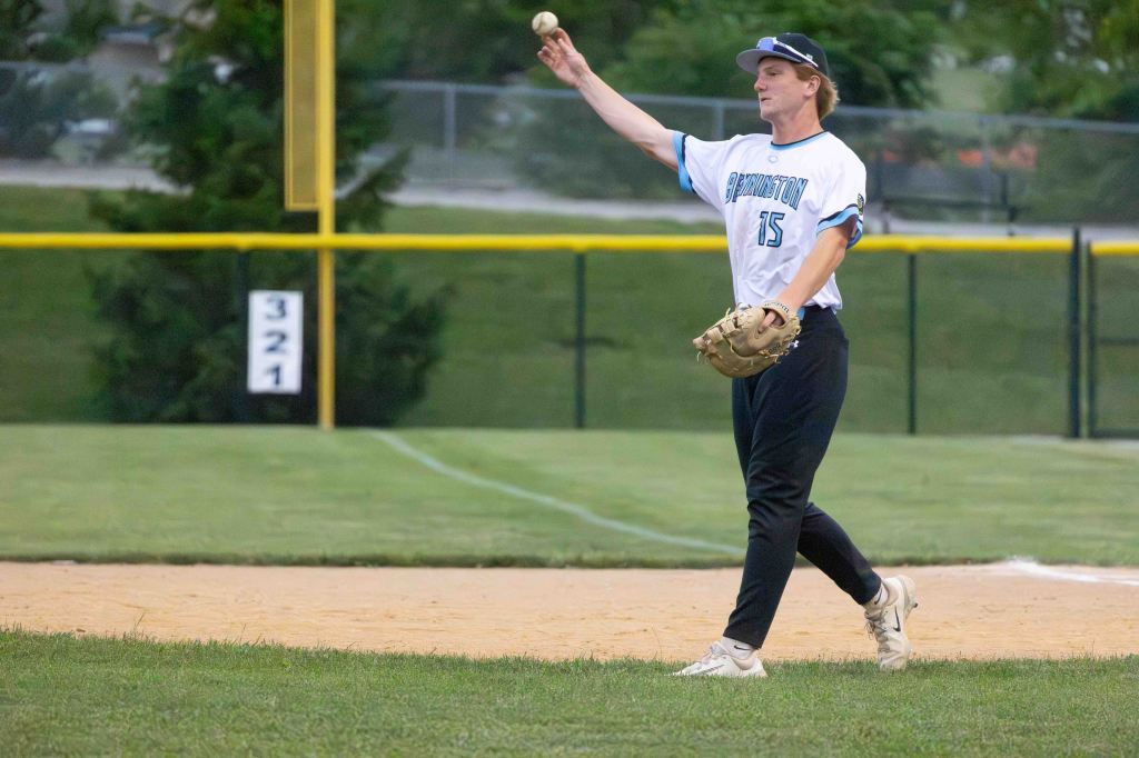 A baseball player in a white and blue uniform throws a baseball from the infield during a game.
