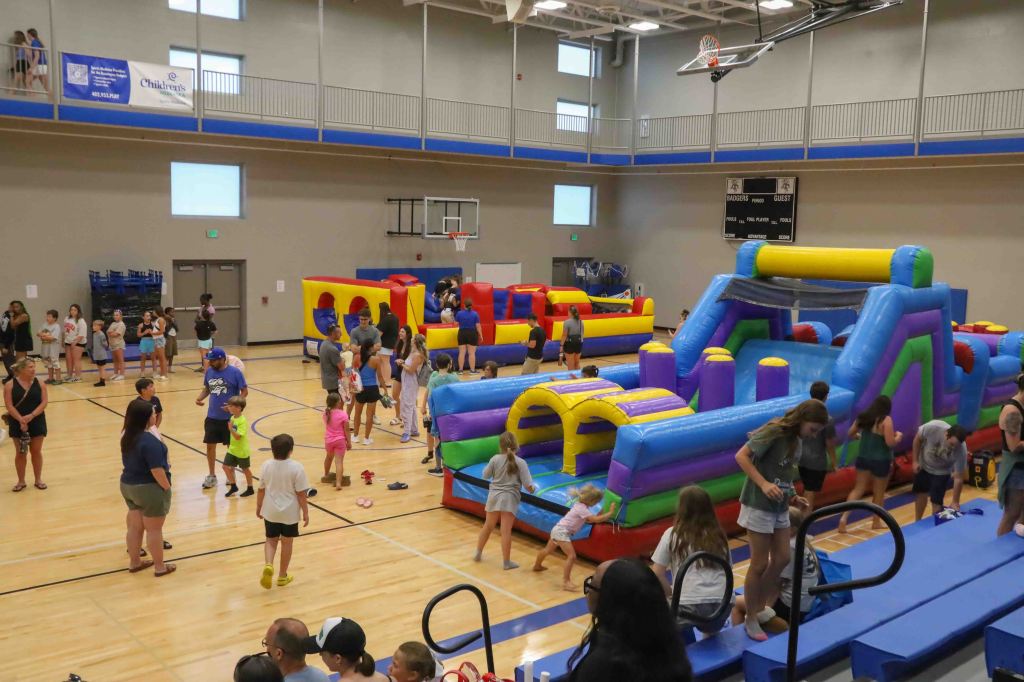 A bustling indoor gym with various colorful inflatable bounce houses and obstacle courses, filled with children and adults engaging in play.