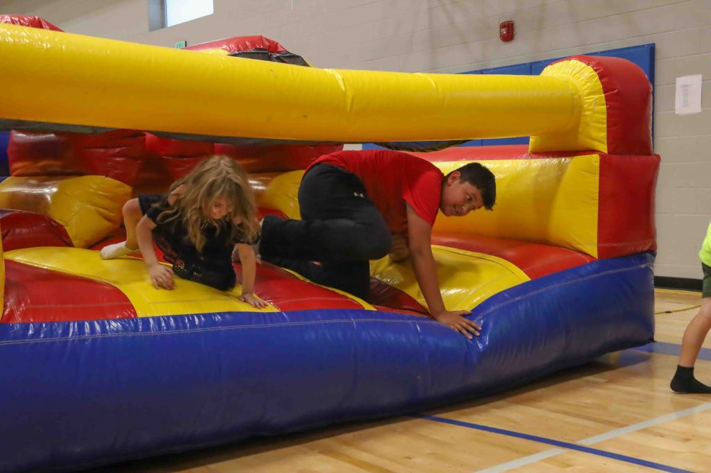 Two children playing on a colorful inflatable bounce house, with one child climbing over a barrier and another kneeling down on the inflatable surface.