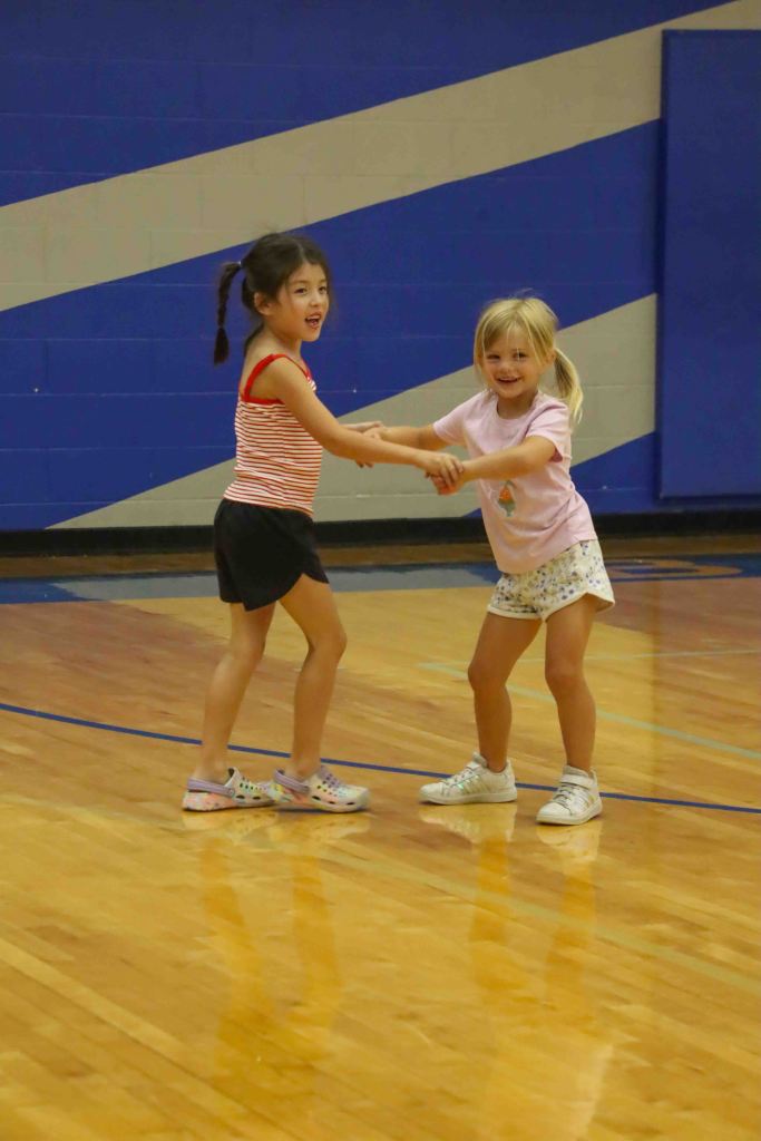 Two young girls holding hands and laughing while playing together on a basketball court.