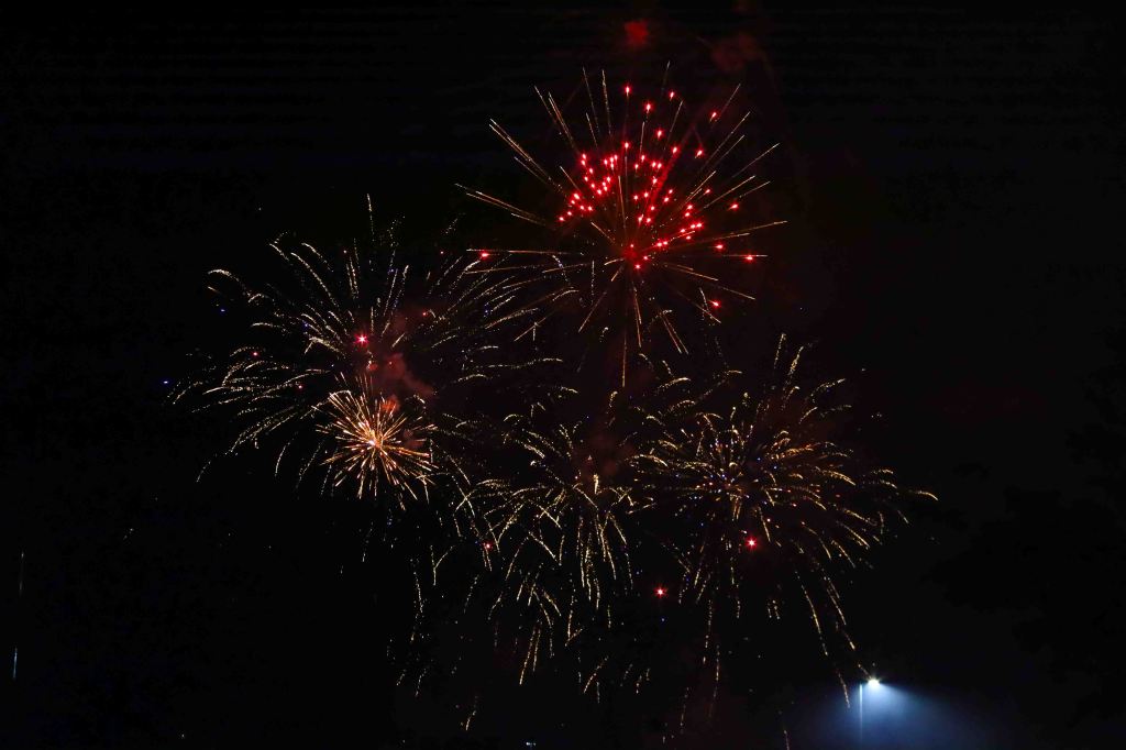 Colorful fireworks exploding in the night sky, featuring bright red and golden bursts against a dark background.