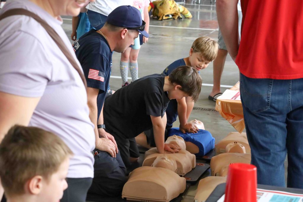 Children practicing CPR on mannequins with an adult supervising