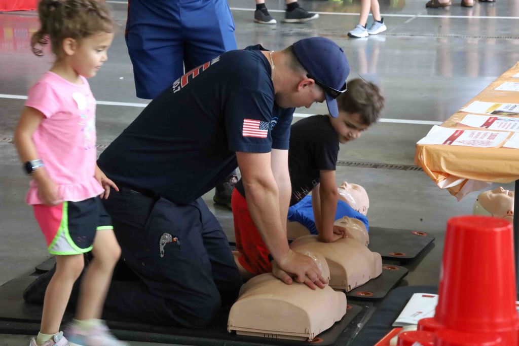 A firefighter teaches children how to perform CPR on mannequins during a safety training event.