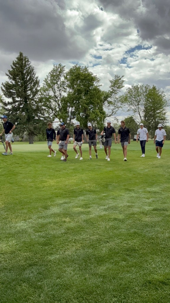 A group of golfers walking on a lush green golf course under a partly cloudy sky.