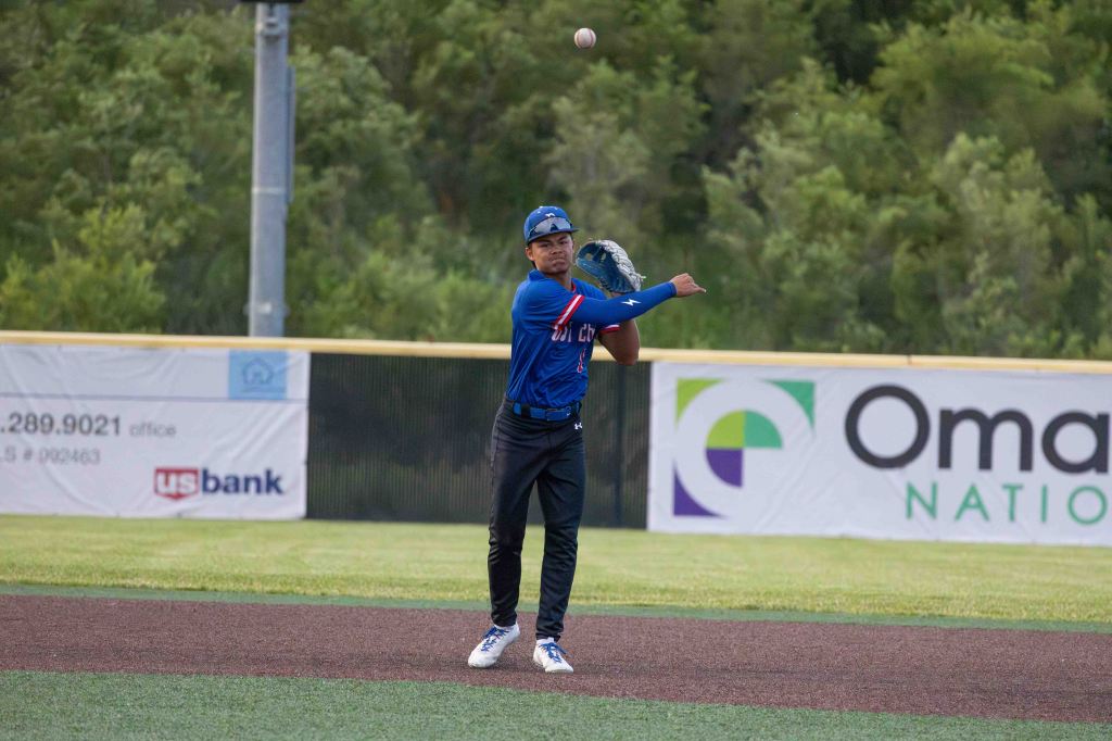 A young baseball player in a blue jersey throws a baseball from the outfield towards the infield during a game.