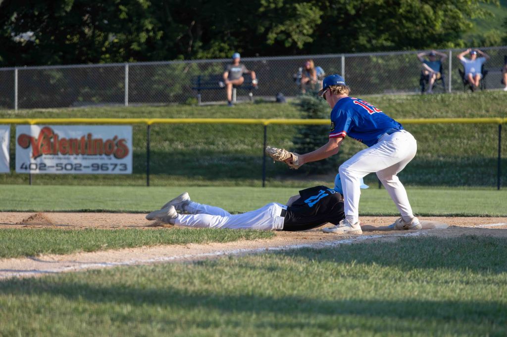 A baseball player in a blue jersey attempts to tag out a player in black who is sliding into base during a game.