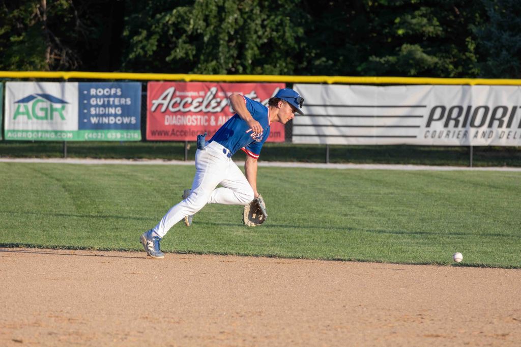A baseball player in a blue uniform fields a ground ball on a diamond during a game.
