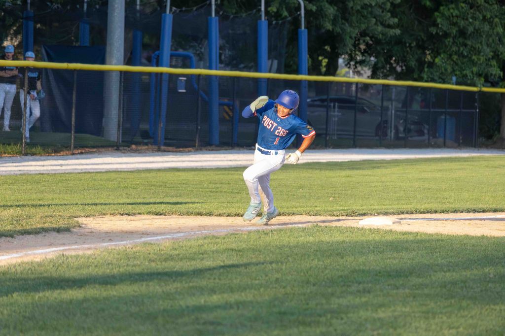 A young baseball player in a blue jersey with 'POST 268' written on it, running towards home plate on a well-maintained baseball field.