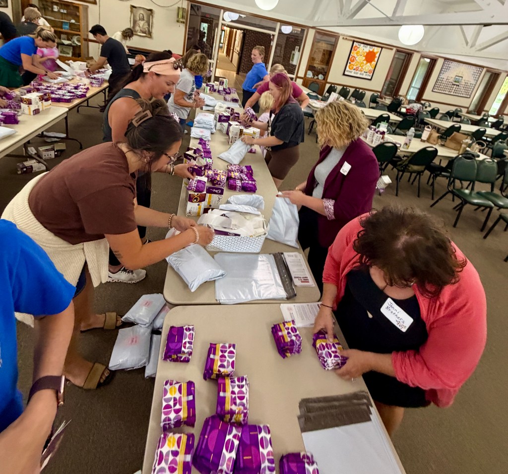 A group of individuals working together at tables, assembling and packaging items in a community space.