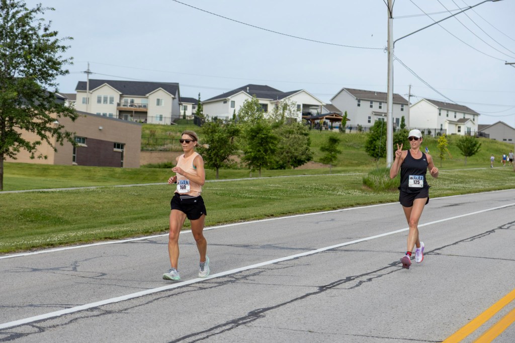 Two female runners participating in a race on a residential street, with houses and trees in the background.