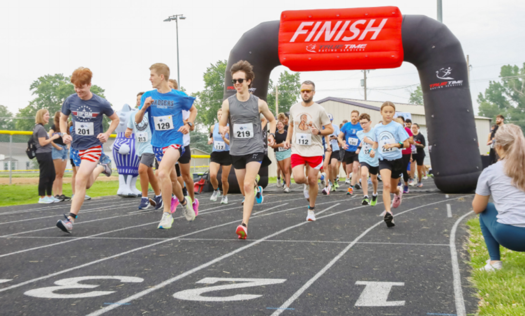 Runners starting a race under a large inflatable finish arch with the word 'FINISH' displayed, on a track surrounded by spectators.