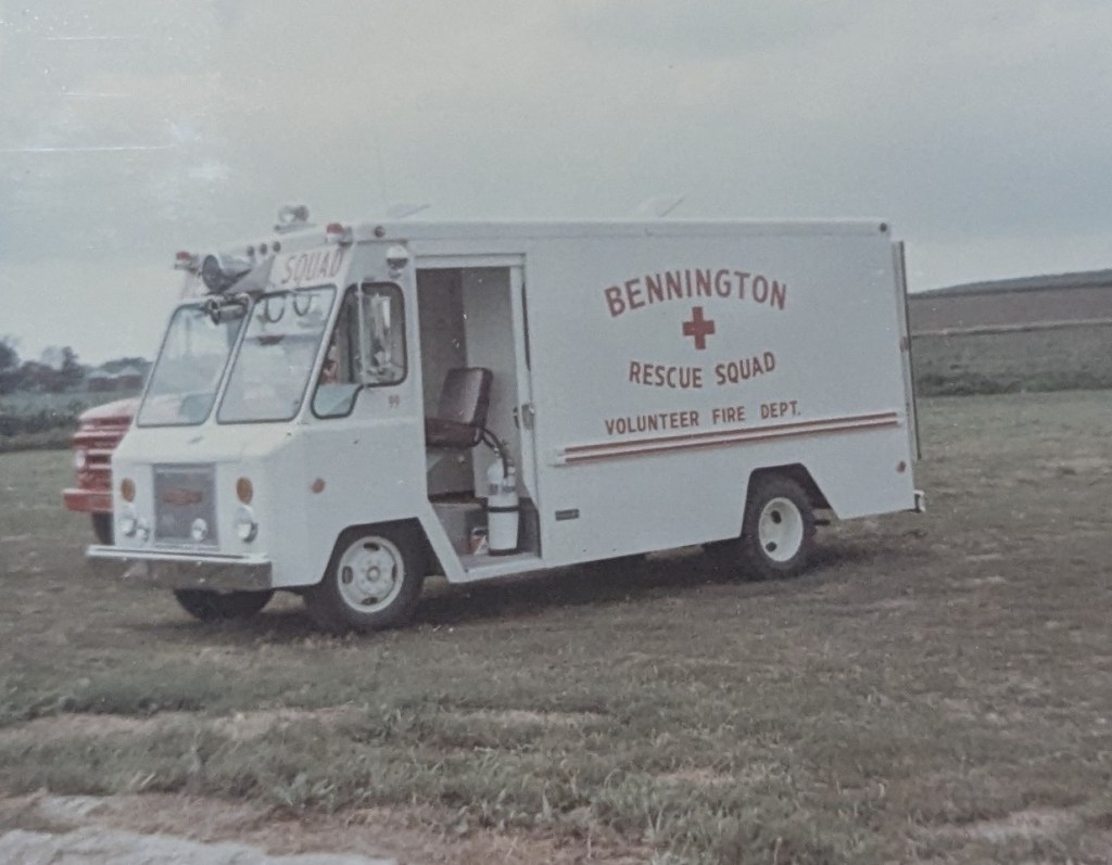 A vintage white rescue squad truck with red lettering that reads 'Bennington Rescue Squad' and 'Volunteer Fire Dept.' parked on a grassy field.