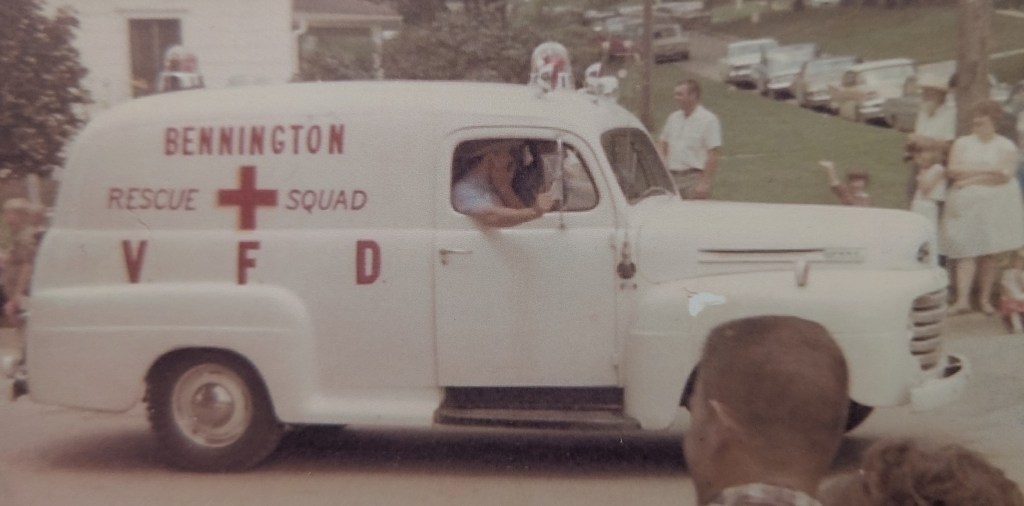 A vintage rescue squad vehicle from Bennington, labeled 'VFD' and 'Rescue Squad,' driving in a parade with spectators in the background.