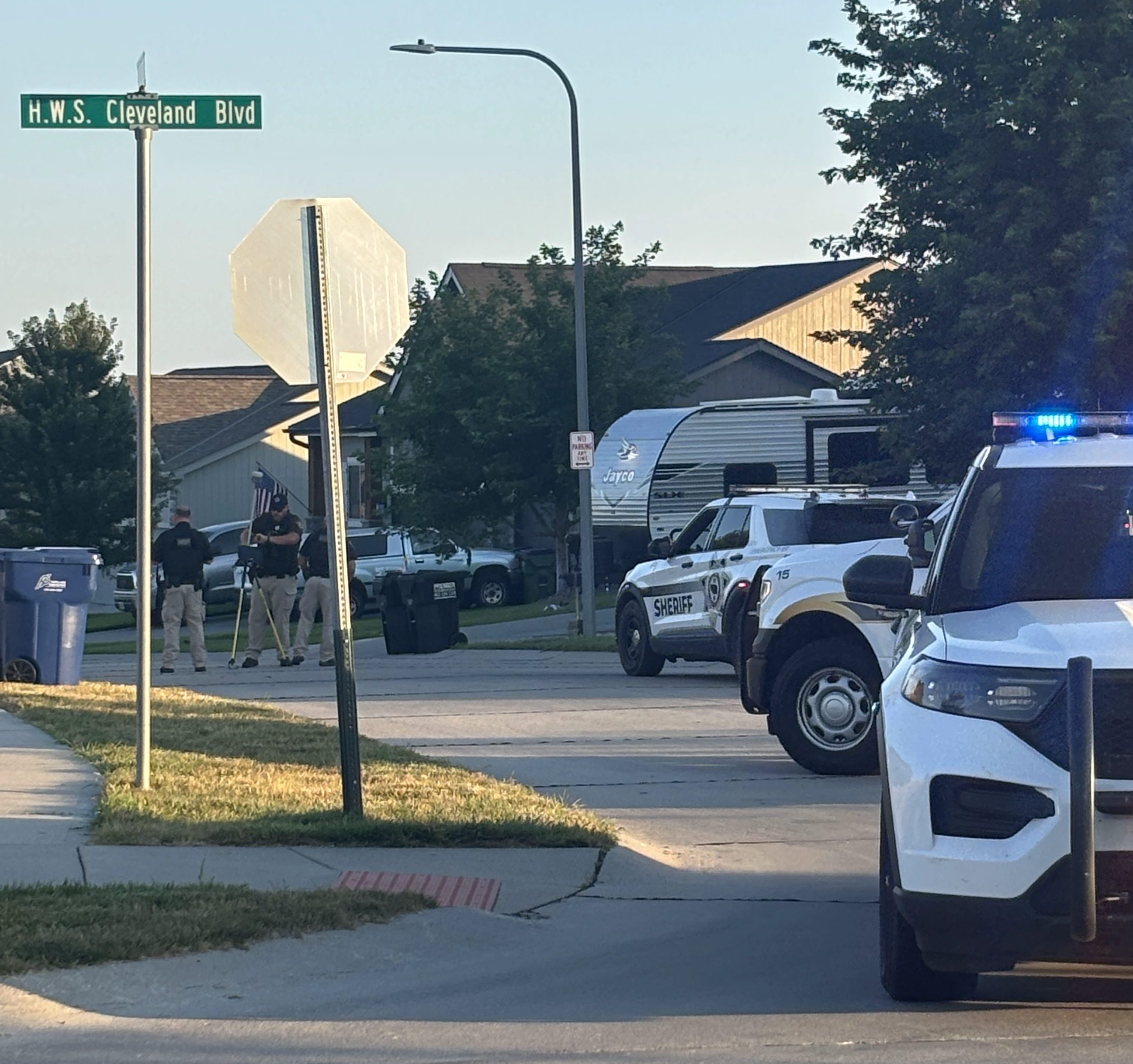 Police vehicles on a suburban street, with officers conducting an investigation near a stop sign and a street sign reading H.W.S. Cleveland Blvd.