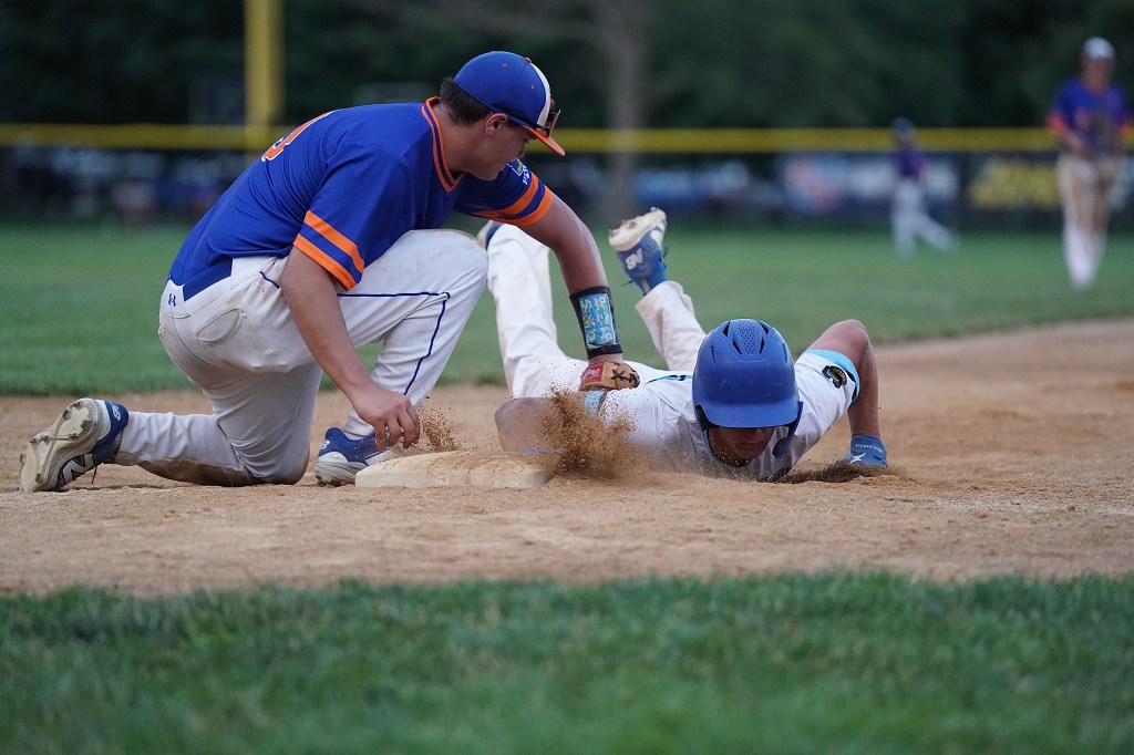 A baseball player sliding into base while another player attempts to tag him, with dust kicked up from the ground.