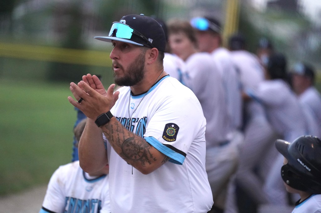 A baseball coach in a team uniform, showing enthusiasm and encouraging players from the dugout during a game.