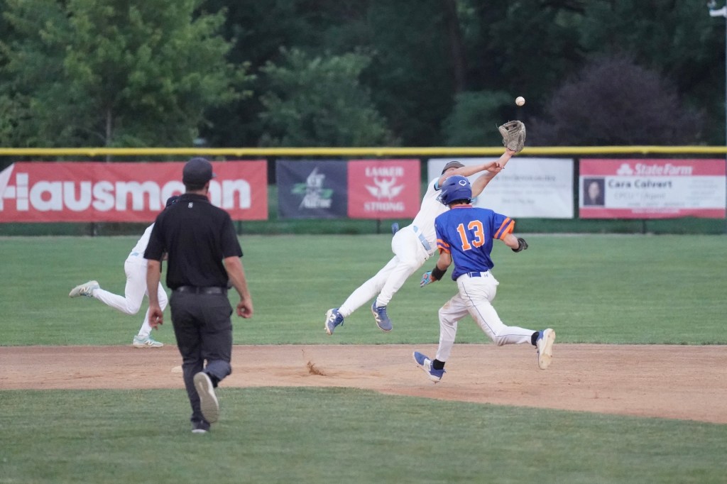 Baseball players in action during a game; one player is leaping to catch a ball while another runs towards the base.